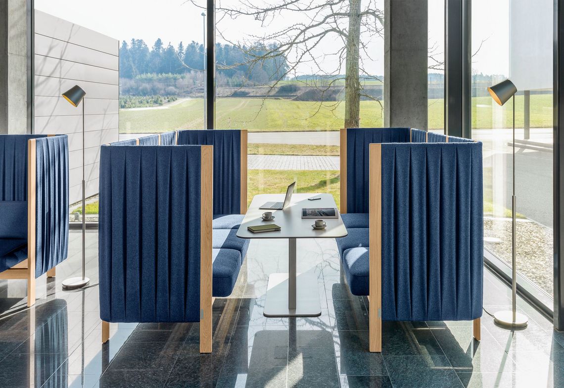 Arbeitstisch mit Vollkernplatte und zwei Dreisitzer in blau gepolstert in der Empfangshalle